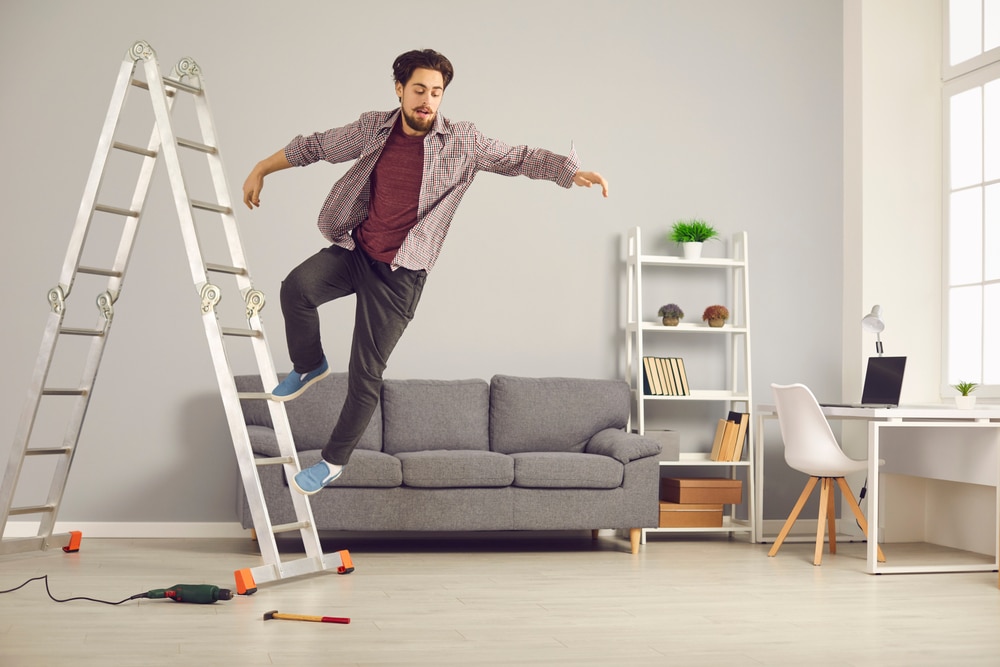 Man losing balance while climbing a ladder in a living room setting, illustrating potential slip and fall hazards in home environments.